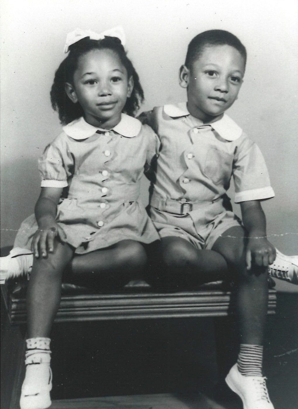 Studio portrait of two small children, a girl with a bow and a boy, seated together