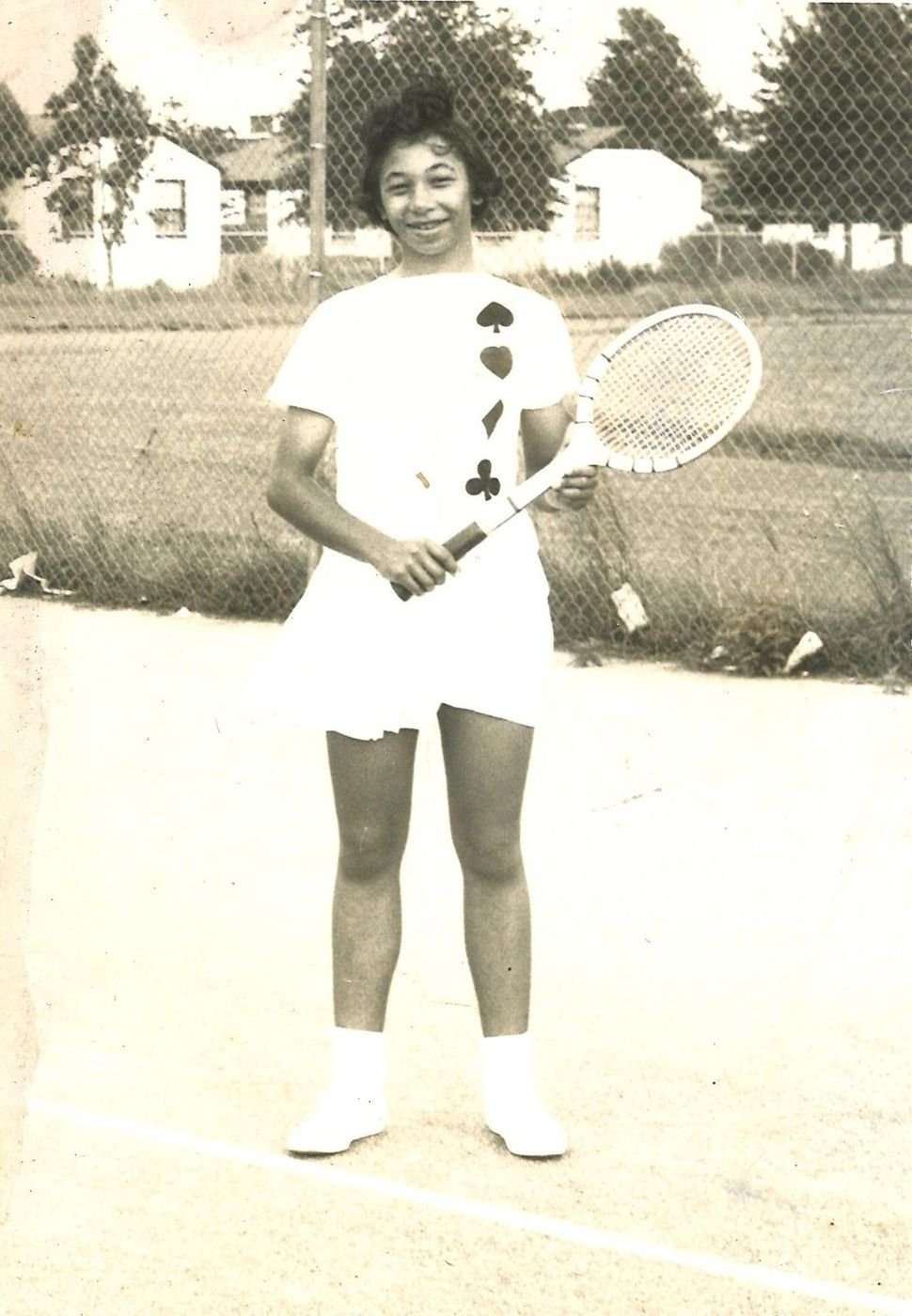 Carolyn Williams as a teenager standing on a tennis court holding a wooden racket