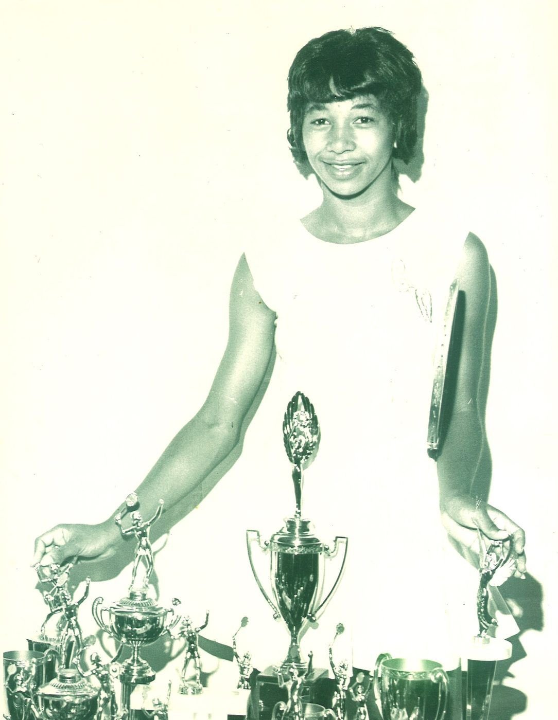 Young Carolyn standing behind a table crowded with tennis trophies