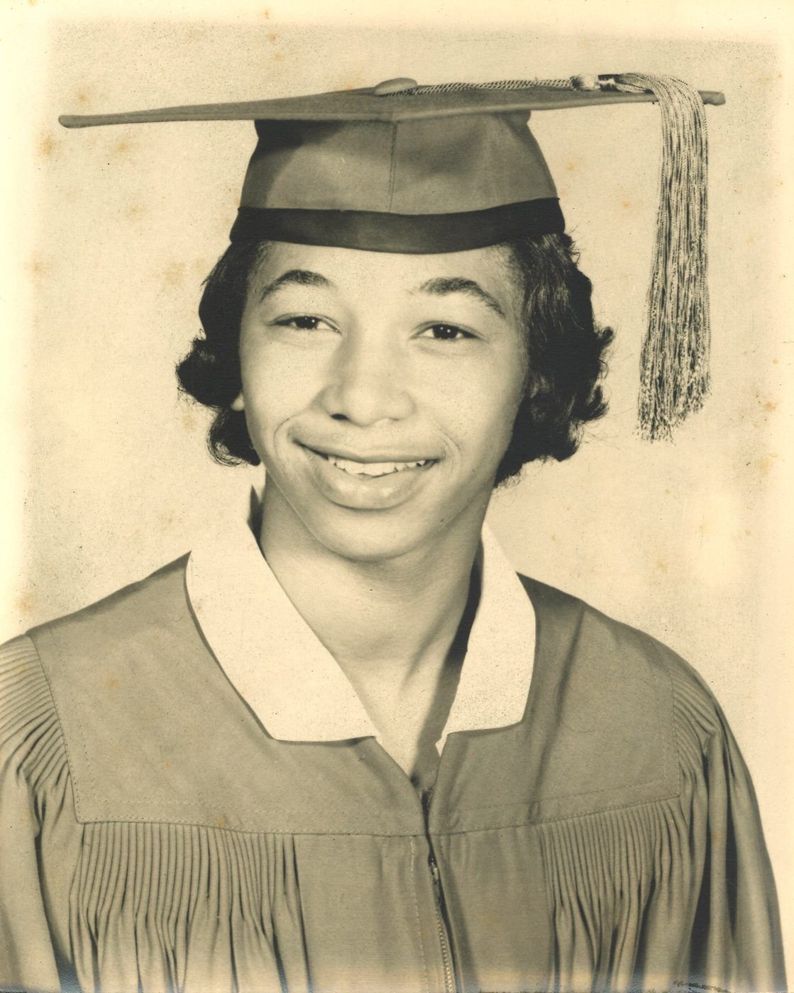 Carolyn's high school graduation portrait in cap and gown, smiling