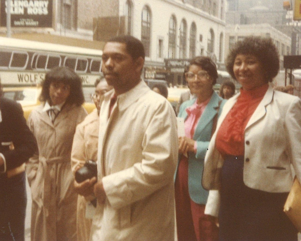 A group on a New York street, Carolyn in a red blouse and white jacket at right, a Broadway marquee behind