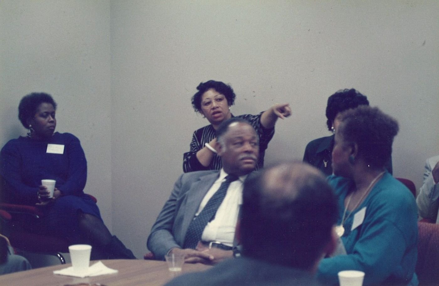 Carolyn standing and pointing while speaking to a seated group in a meeting room