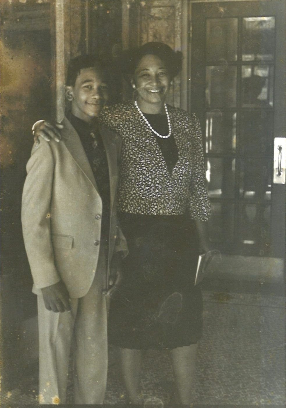 Carolyn in a patterned jacket and pearls with teenage Marcus in a suit