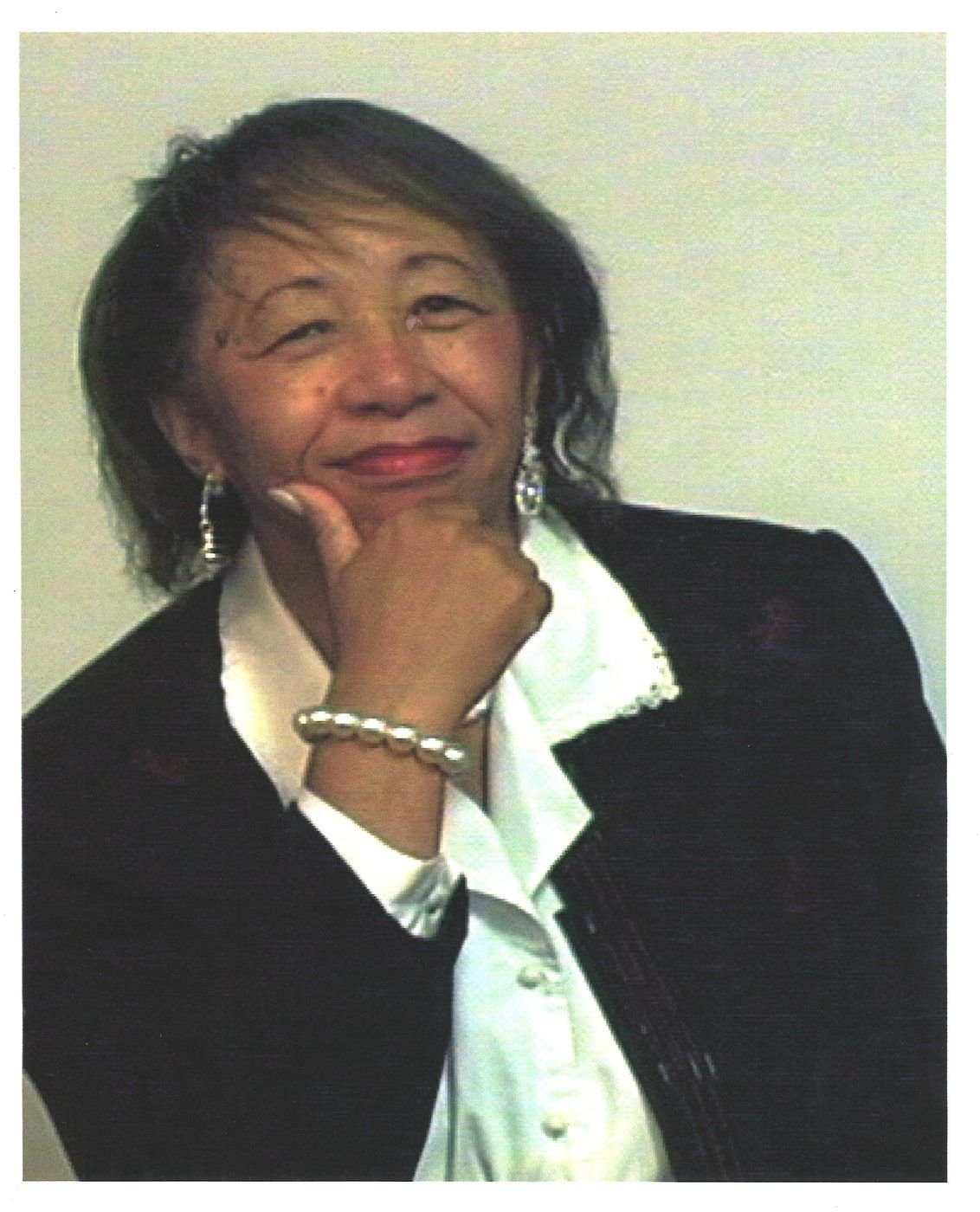 Portrait of Carolyn in a dark suit and white blouse, hand on chin, pearl bracelet