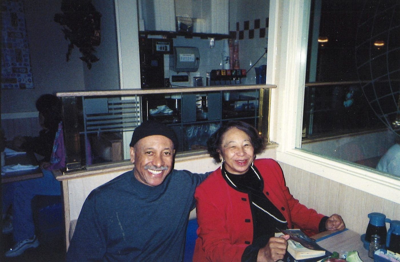 Carolyn in a red jacket smiling beside a man in a cap at a diner table