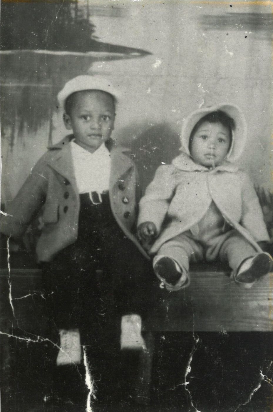 Two small children in winter coats in an old damaged black and white studio print