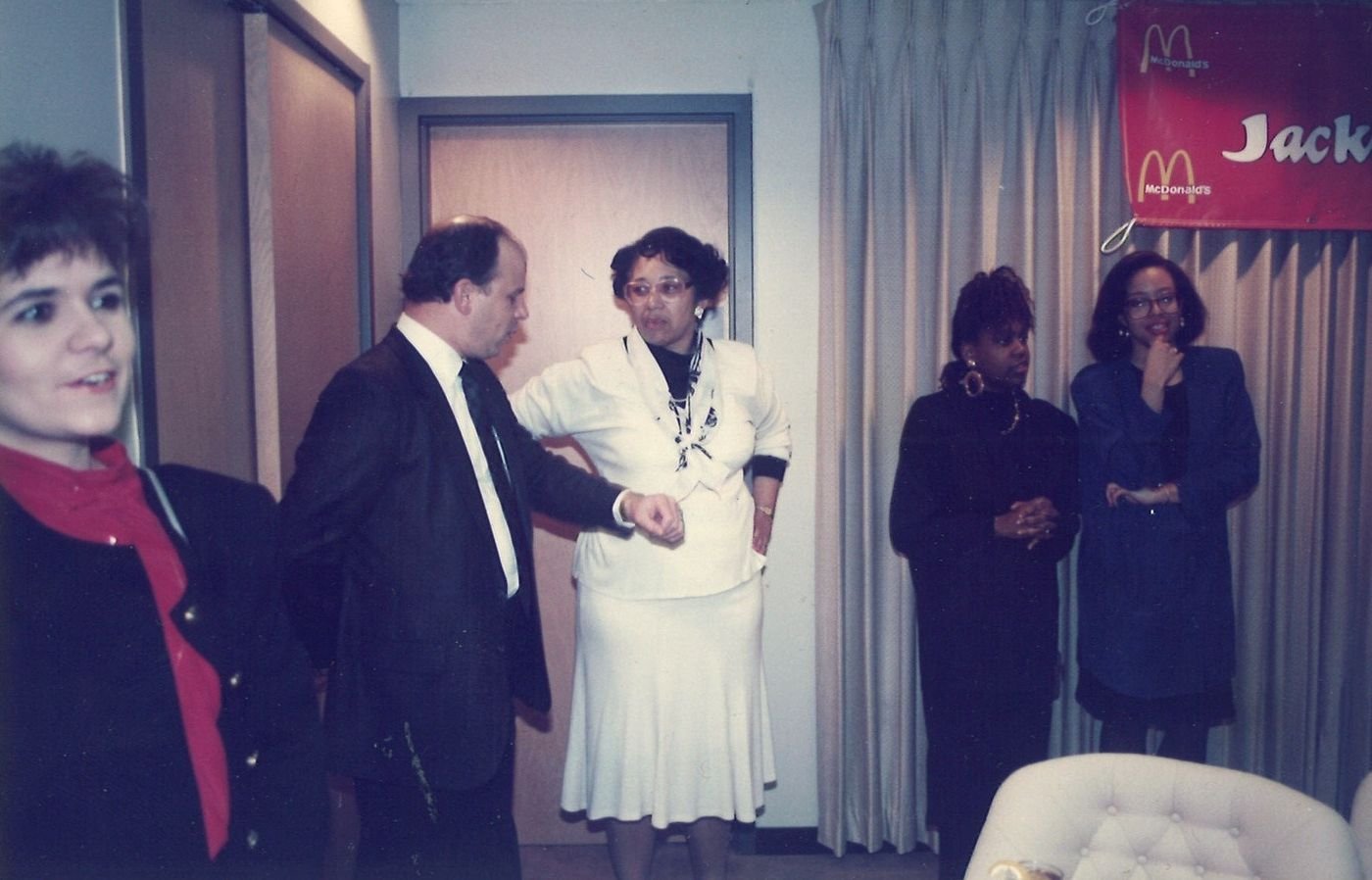 Carolyn in a white suit greeting people at an indoor event