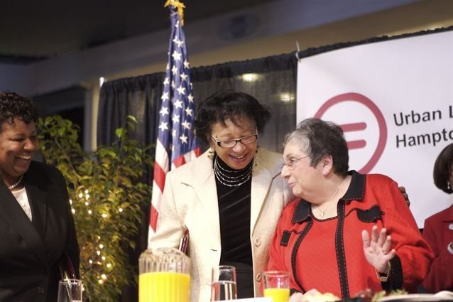 Carolyn leaning in and laughing with a woman at an Urban League table